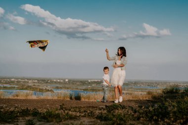 Genç esmer anne gün batımında 3 yaşındaki oğluyla uçurtma fırlatıyor.