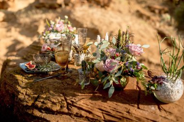 Doğada kırsal tarzda bir düğün masası, cam süsleme, taze çiçekler ve okaliptüs dalları.