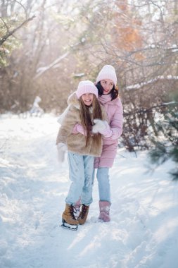10 yaşındaki tatlı kıvırcık kız ve genç annesi kışın karlı ormanda oynuyorlar.