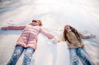 10 yaşındaki tatlı kıvırcık kız ve genç annesi kışın karlı ormanda oynuyorlar.