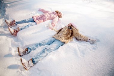 10 yaşındaki tatlı kıvırcık kız ve genç annesi kışın karlı ormanda oynuyorlar.