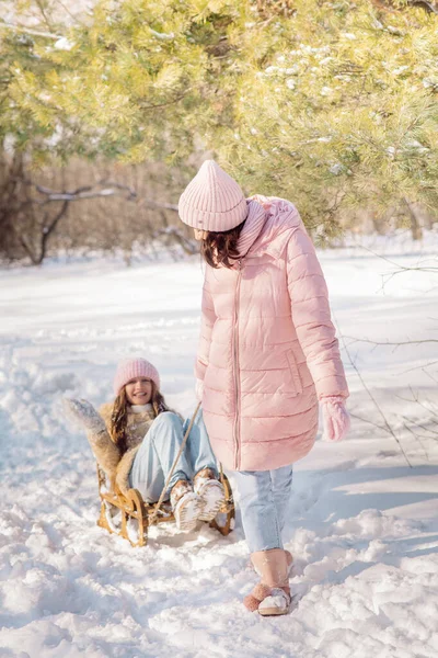 10 yaşındaki tatlı kıvırcık kız ve genç annesi kışın karlı ormanda oynuyorlar.