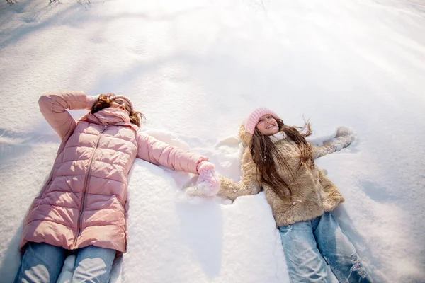 10 yaşındaki tatlı kıvırcık kız ve genç annesi kışın karlı ormanda oynuyorlar.