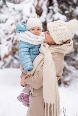 Annem küçük kızını kış ormanında yürüyüşe çıkarırken kollarında tutuyor.