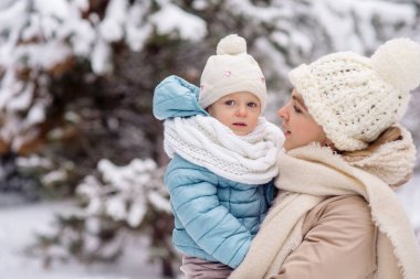 Annem küçük kızını kış ormanında yürüyüşe çıkarırken kollarında tutuyor.