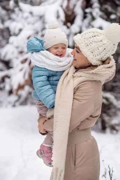 Annem küçük kızını kış ormanında yürüyüşe çıkarırken kollarında tutuyor.