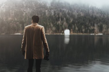 Kahverengi ceketli genç bir erkek fotoğrafçı küçük aynasız bir kamerayla fotoğraf çekiyor.