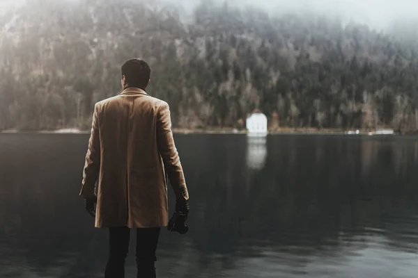 Kahverengi ceketli genç bir erkek fotoğrafçı küçük aynasız bir kamerayla fotoğraf çekiyor.