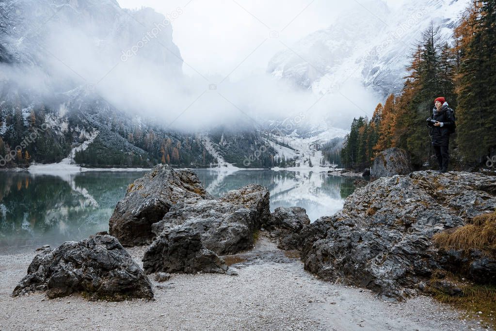 Evening view of Lago di Braies (Braies lake, Pragser wildsee) during fog, big rocks in foreground with a person standing on top
