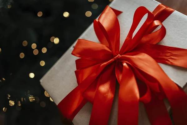 Big Christmas gift box with big red bow. Out of focus Christmas tree in background.