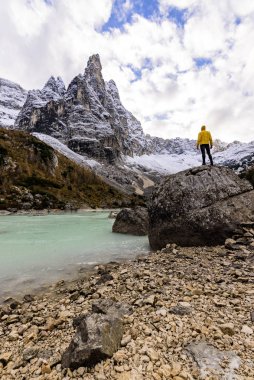 Sarı ceketli bir erkek gezgin büyük bir kayanın üzerinde duruyor, İtalyan Alplerinde Sorapis Gölü. 