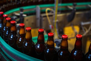 Bira fabrikasında / kırmızı başlıklı (yüksek Iso görüntülü) taşıyıcı banttaki bira şişeleri)