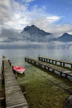 Traunsee Gölü üzerinde tahta köprüsü olan ahşap kayıkhane. Arka planda alçak bulutlarla kaplı Traunstein zirvesi. Avusturya, Alp Bölgesi..