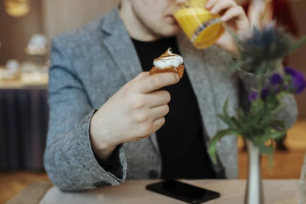 Man drinking fresh orange juice and eating a cupcake in restaurant. Modern smartphone on the table.