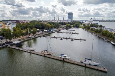Rıhtımdaki birden fazla yat ve teknenin havadan görüntüsü. Arka planda büyük bir yolcu gemisi.