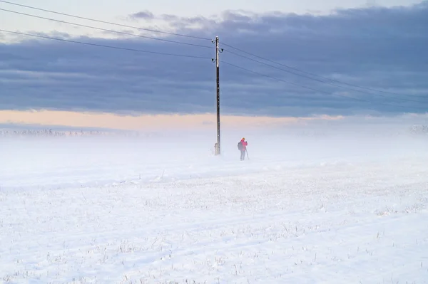 Winter sunrise over snow covered field with a layer of fog and a person in distance