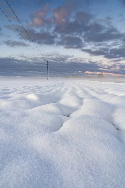 Winter sunrise over snow covered field with round shape snow piles .