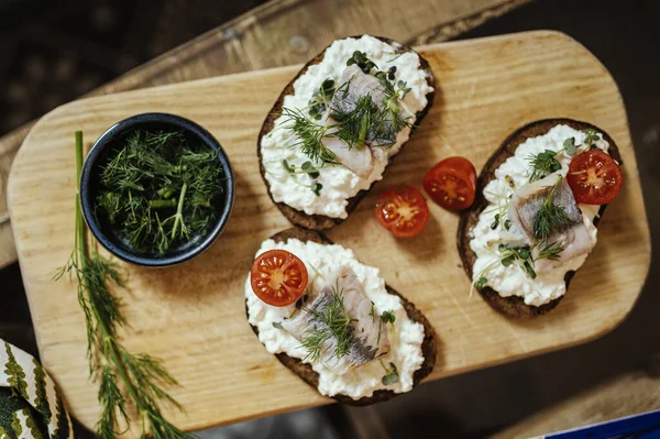 Süzme peynirli esmer ekmek ve tahta tabakta ringa balığı..
