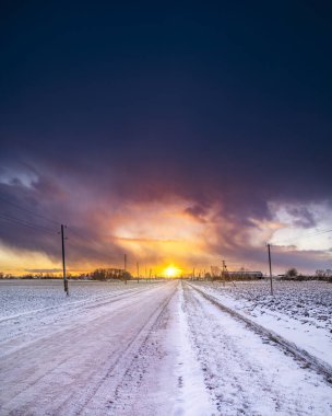 Fırtınalı gökyüzüyle kaplı karların üzerinde renkli günbatımı gökyüzü.