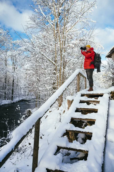 身穿红色夹克的男性摄影师拍摄雪地森林冬季风景的照片 — 图库照片