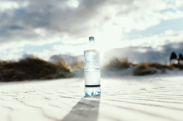 Plastic water bottle on a sea sand background during bright summer day