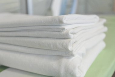 Ütü masasında yeni yıkanmış beyaz çarşaf yığını, arka planda ütü.