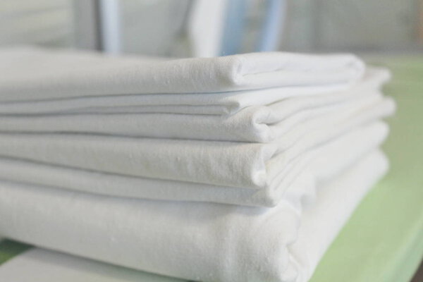 A stack of freshly washed white linen on an ironing board, an iron in the background