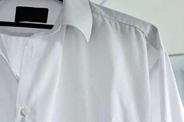 White men\'s shirt on a hanger close up. Clean clother, ironong concept. White shirt hanging after washing. Housekeeping