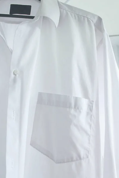 White men\'s shirt on a hanger close up. Clean clother, ironong concept. White shirt hanging after washing. Housekeeping