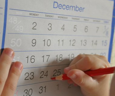 Kırmızı kalemle Noel takviminde daireler çizen bir çocuk. Tatilin başında, yeni yıl arifesinde. Uyarı takvimi, planlama, bir mucize beklentisi