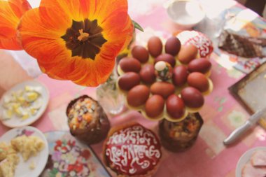 Ortodoks Paskalyasında hayat devam ediyor. Masadaki vazoda bir lale ve arka planda Paskalya pastaları, paskalya kırmızı yumurtaları. İsa dirildi. Seçici odak