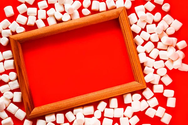 一个木制相框 周围散布着白色的小棉花糖 红色背景 — 图库照片