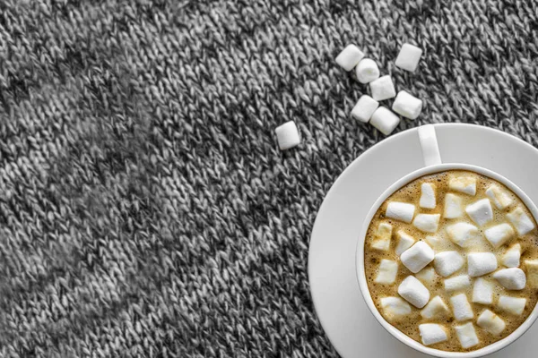 A Cup of coffee with marshmallows on a gray background. Next to the Cup are some marshmallows