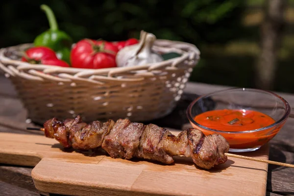 Grilled kebab with vegetables and red sauce on wooden table — Stock Photo, Image