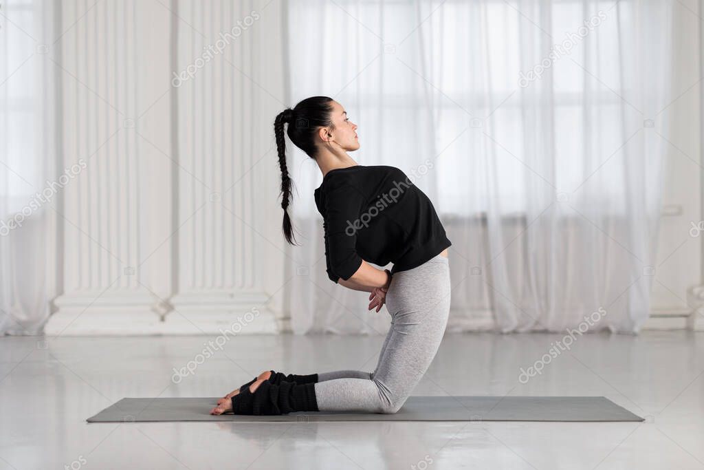Young asian woman doing yoga exercise on gray mat, stretching and preparing for standing in Ustrasana, Camel Posture.