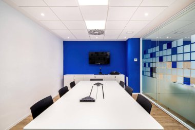 Masayla, sandalyelerle, televizyonla modern ofis içinde mavi ve beyaz duvarlarla sohbet için boş toplantı odası.