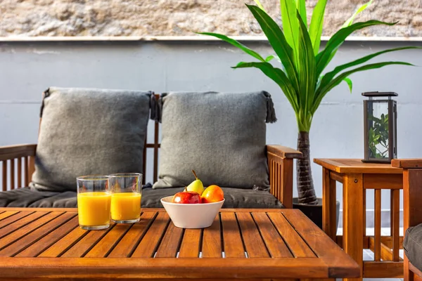 Terrasse mit Holztisch, Sofa und Stühlen. Obst und Orangensaft am Tisch. Gesundes Frühstück zu Hause. — Stockfoto