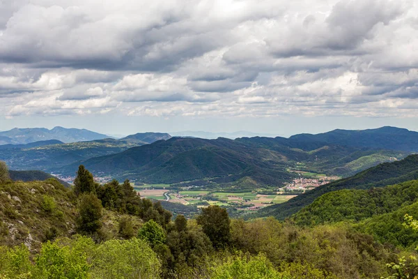 Heavy clouds hanging over mountains covered by the forest and village at the bottom. Nature landscape.