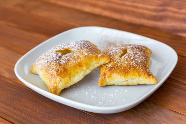 Tahta masadaki beyaz tabakta pudra şekeri ve tarçın serpiştirilmiş tatlı çörekler. Taze fırın ürünü..