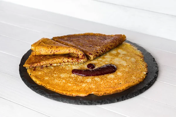 Süße Crêpes, dünne Pfannkuchen mit Fruchtmarmelade auf einem schwarzen Steinteller. Holzuntergrund. Seitenansicht. — Stockfoto