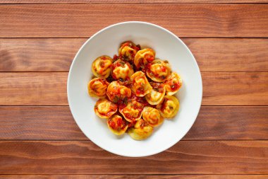 Geleneksel Rus yemeği pelmeni, domates soslu etli börek, beyaz tabakta, ahşap arka planda..