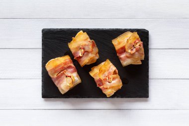 Kızarmış pastırmaya sarılı Ravioli, siyah taş tabakta kanepe, beyaz ahşap masa..