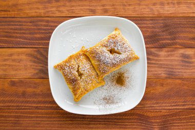 Taze pişmiş tatlı çörekler üzerine pudra şekeri serpiştirilmiş ve beyaz tabakta tarçın serpiştirilmiş ahşap masa, üst manzara