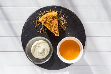 Beyaz ahşap arka planda siyah taş tabakta ekşi kremalı ev yapımı ballı kek. Üst görünüm