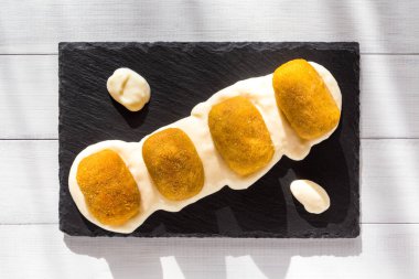 Ahşap zemin üzerinde siyah taş tabakta beyaz soslu kızarmış et kroketleri. Sağlıksız yiyecekler. Üst görünüm