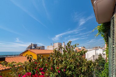 Güneşli bir günde Costa Brava sahilinin balkonundan manzara. Döşemeli çatılar, yeşil bitkiler ve çiçekler, mavi gökyüzü ve deniz.