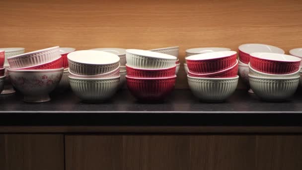 Červené a bílé keramické misky v dřevěné kuchyňské skříni. Stolní nádobí osvětlené shora ve skříni moderního interiéru