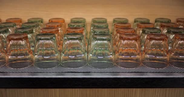 Vasos de diferentes colores en gabinete de cocina de madera. Vasos transparentes para agua o jugo . — Vídeo de stock