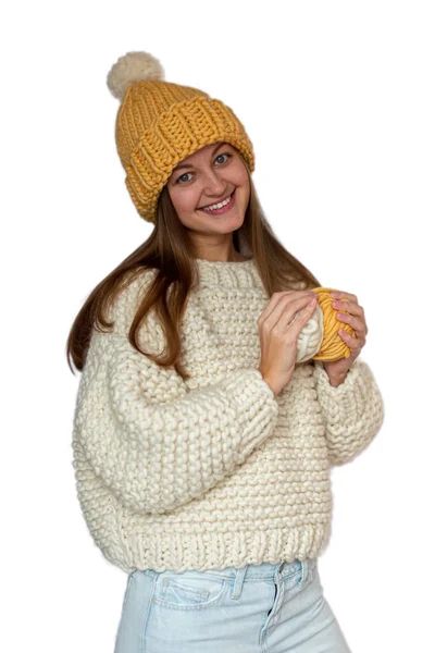 Beautiful happy girl holding in her hands two yarn balls and wearing a sweater and cap, knitted thick thread. Handmade winter clothes. Isolated. — Stock Photo, Image