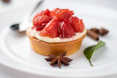 Çilekli kek ve tarçınlı, ve beyaz bir tabakta yeşil bir yaprak ve kaşıkla